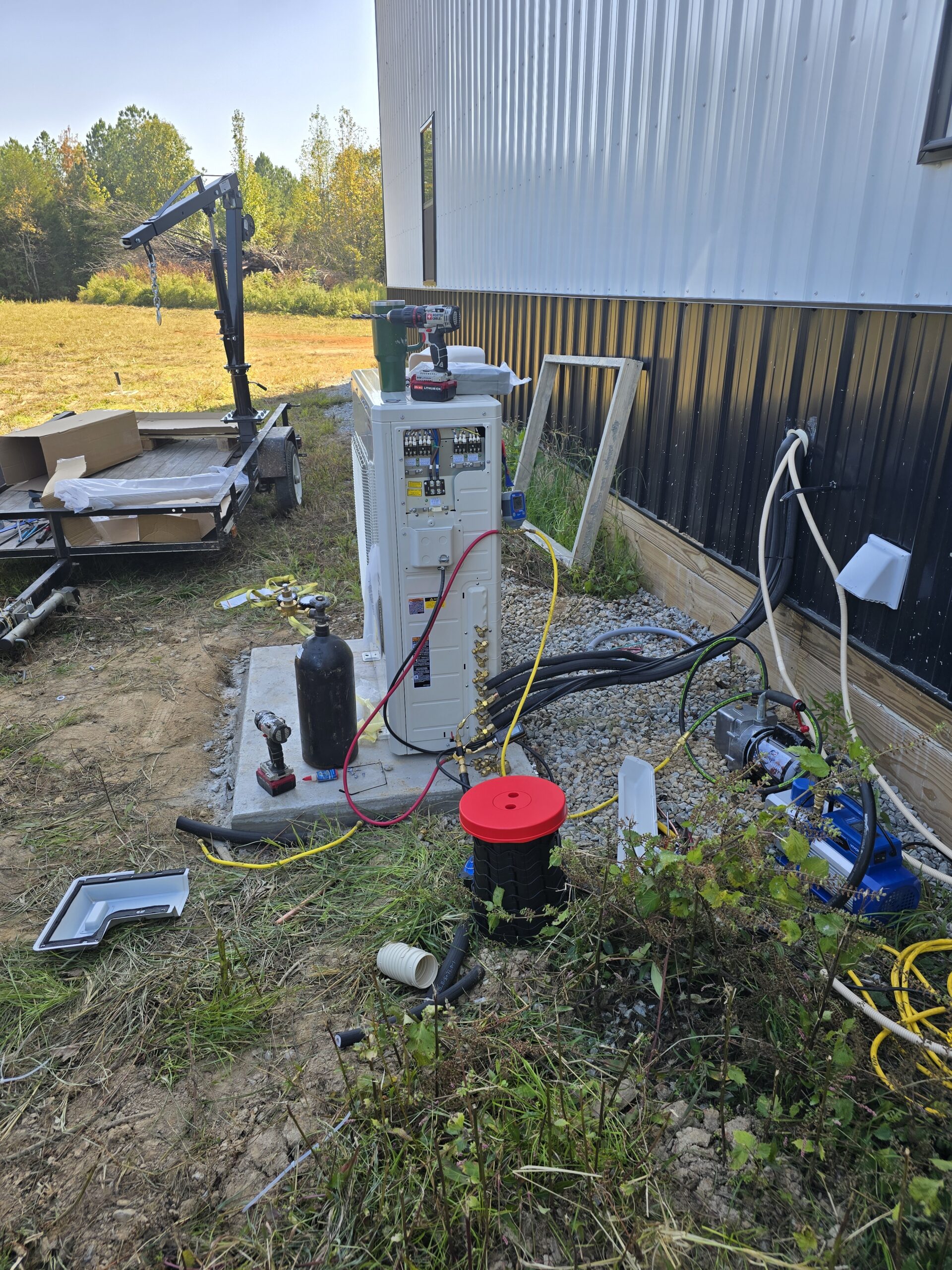 Outdoor HVAC unit installation with tools and equipment scattered on the ground beside a building.