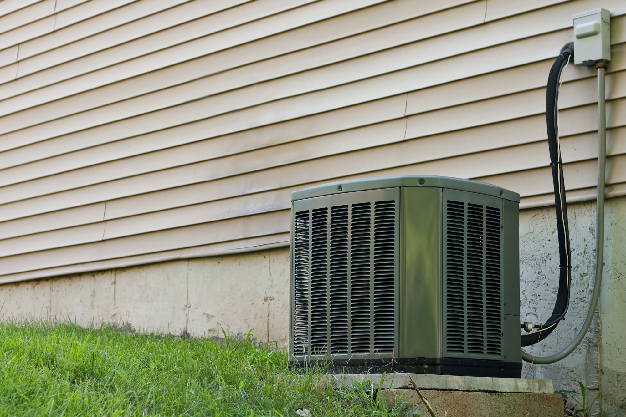 A heating installation complements the air conditioning unit, both securely placed on a concrete slab beside the house with its classic vinyl siding.